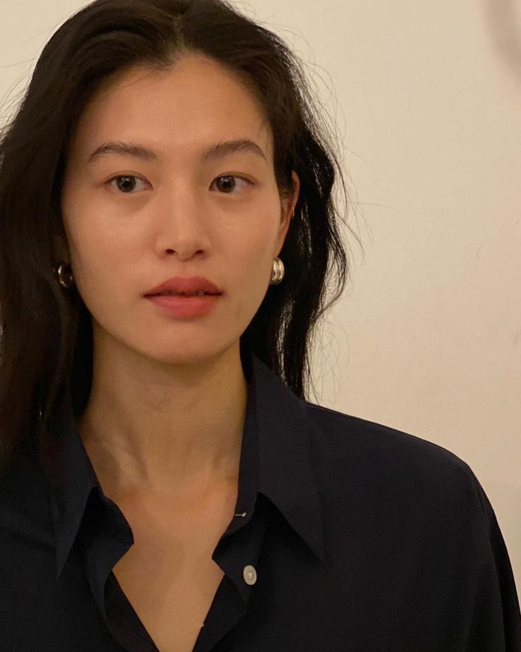 a portrait of an asian woman with dark hair wearing a black buttondown shirt and silver earrings. she is facing the camera with a neutral expression against a neutral background. the shot is framed from the head and shoulders.