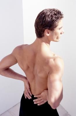 a man is shirtless and standing in a pose with his left hand on his hip and his right hand on his back. he is wearing black pants. the man has short brown hair. the background is white.
