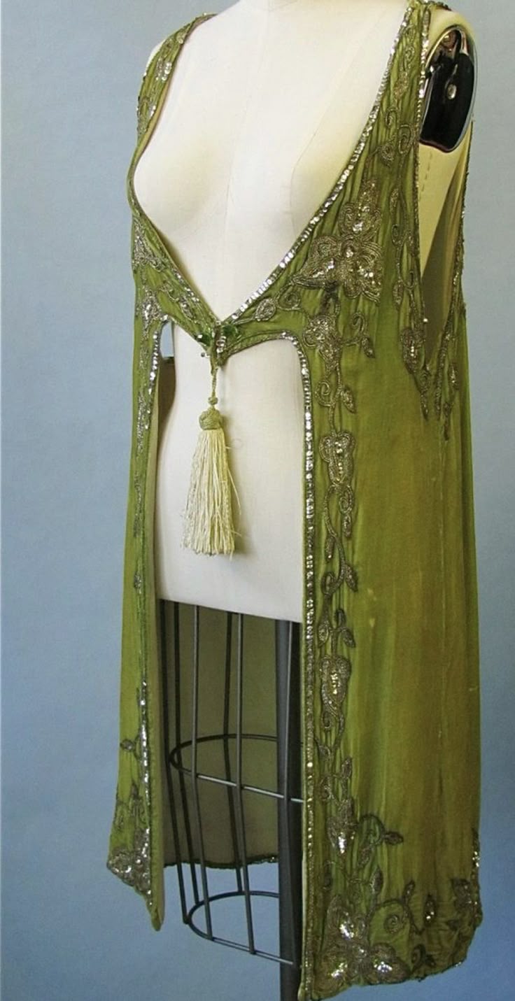 a sleeveless green dress with a tassel is displayed on a mannequin. the dress is decorated with beads. it appears to be a vintage piece.
