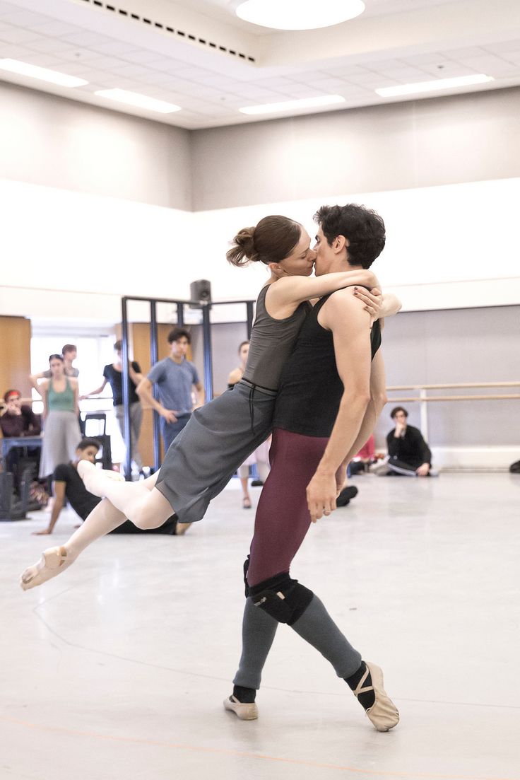 a male and female ballet dancer in a studio rehearsal. the male dancer holds the female dancer, who
