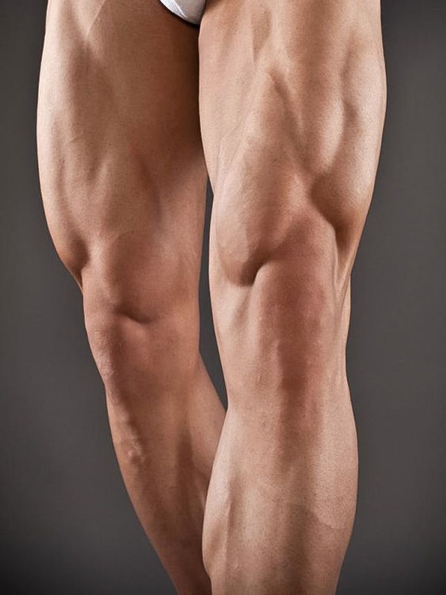 the image showcases the muscular legs of a male bodybuilder. the focus is on the definition and size of his thigh muscles, particularly the quadriceps and hamstrings. the image is taken against a neutral gray background, highlighting the physique of the subject.