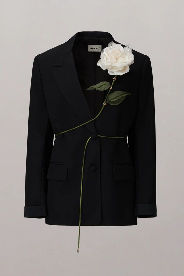 a black blazer is displayed with a large white rose embellishment attached to the lapel and extending down the front, creating a decorative design across the jacket.