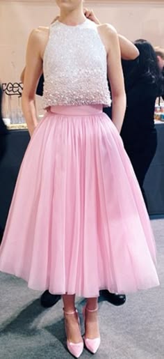 a young woman wearing a beautiful pink tulle skirt and a white sequined top. she is standing with her arms at her sides. the dress is perfect for a special occasion, such as a prom or wedding. her pink shoes complete the look.