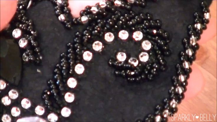 a closeup of black textile embellished with black beads and clear rhinestones. the beads outline the textile and create decorative patterns such as a spiral shape.
