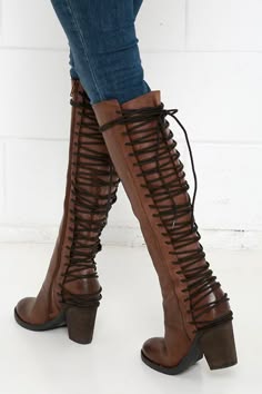 a woman is wearing a pair of brown leather lace up boots. the boots are high heeled and have a chunky heel. the boots lace up the back of the calf. the woman is wearing jeans and the boots are the focal point of the image.