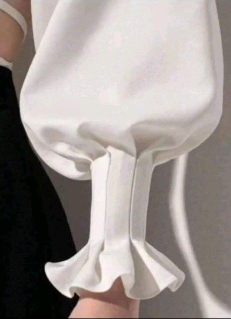 closeup shot of a white blouse sleeve with a puffy style and a ruffled cuff. part of a black garment is visible in the background.