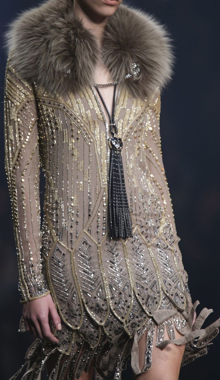 a woman is wearing a glamorous  sequined dress with a fur collar and a tassel necklace. the dress is  beaded and features a fringe hem.  the woman looks elegant and sophisticated. this is an example of high fashion evening wear.