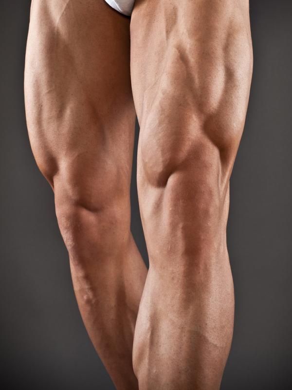 the image showcases the lower body of a muscular man, likely a bodybuilder, from the waist down. his legs, particularly his thighs, display significant muscle definition and vascularity. he wears only white briefs, drawing focus to his physique. the background is a neutral gray, typical of studio photography, and the lighting is even, highlighting the details of his musculature.