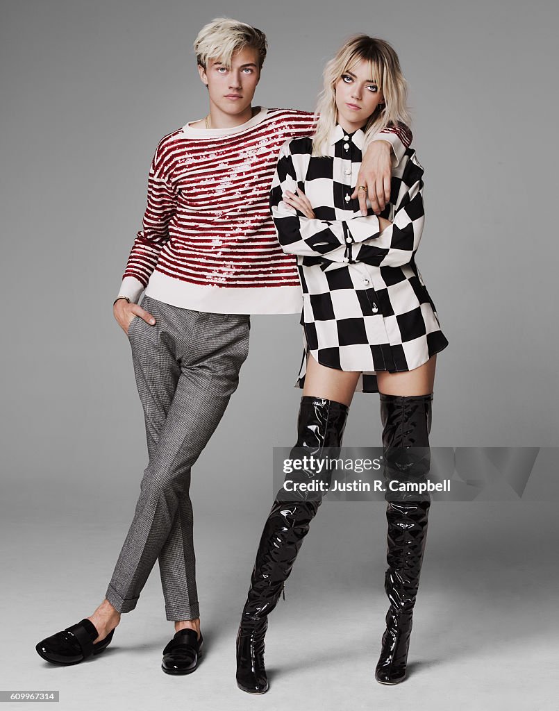 a fulllength studio shot features a man and a woman in fashionable attire against a gray backdrop. the man, with blonde hair, is wearing a red and white striped longsleeved shirt and gray pants. he has his hands in his pockets and is wearing black loafers. the woman, also blonde, is wearing a black and white checkered shirtdress and black patent leather thighhigh boots. she has her arms crossed and is looking at the camera. the man has his arm around her shoulder. the "getty images" watermark and photographer credit are visible.