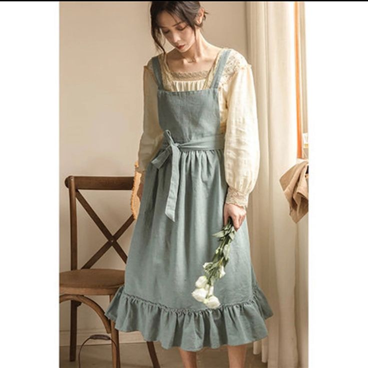 a woman is modeling a vintageinspired, romantic dress. the dress is a dusty teal color with a ruffled hem and a laceup back. she is standing in a room with soft, natural lighting. the overall aesthetic is cottagecore and feminine.