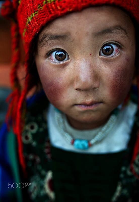 a closeup portrait of a young girl with a red hat, large eyes, and a necklace, displaying an expression of innocence and vulnerability. the image focuses on her face, highlighting her features and attire.