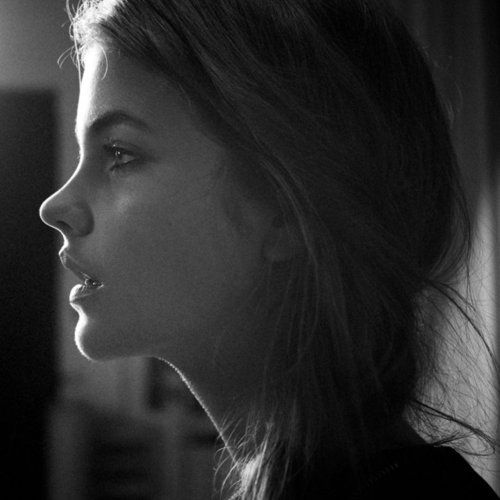 a black and white portrait of a woman's profile. her face is lit from the front, highlighting her features. her hair is long and flowing. she appears to be looking slightly upwards.