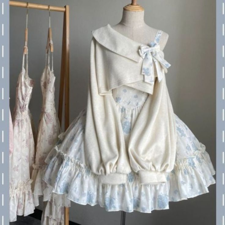 a delicate cream and blue floral lolita fashion dress displayed on a mannequin. the dress features a floral skirt with ruffles, a cropped sweater with a large collar and a bow on the shoulder.