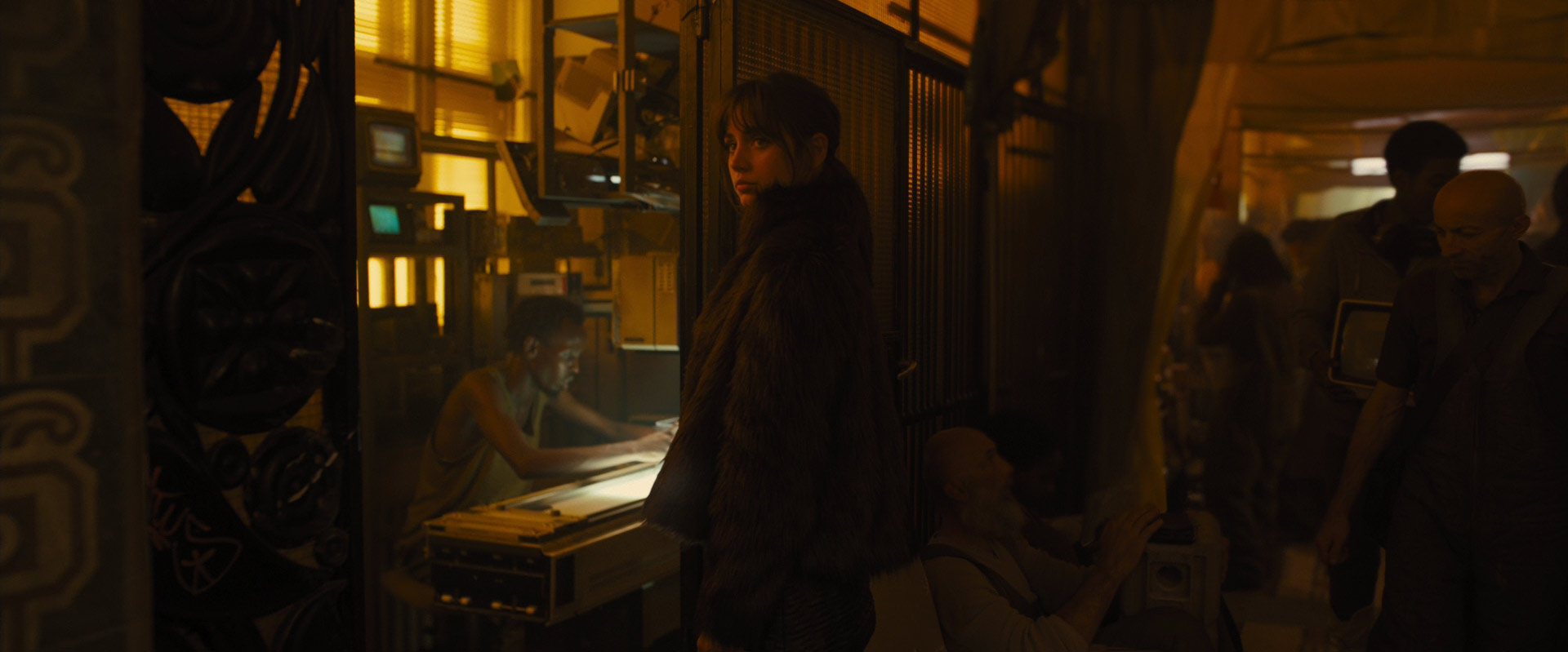 a woman in a dark coat looks intently at the camera, her expression serious and focused. the scene is set in a dimly lit hallway filled with people who are out of focus. the atmosphere is dark, futuristic, and hints at a scifi movie setting.