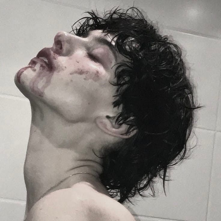 a closeup portrait of a young man with blood on his face. his eyes are closed and he is looking up. the image is dark and dramatic, and the man's expression is intense and mysterious.