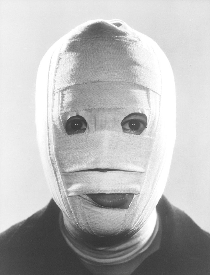 a man with his entire face bandaged. he appears to be in pain and suffering.  the image is black and white, and the man's face is the focal point of the image.  the bandages are very tight and are covering the man's entire face, only leaving his eyes visible. he is looking at the camera with a fearful expression.