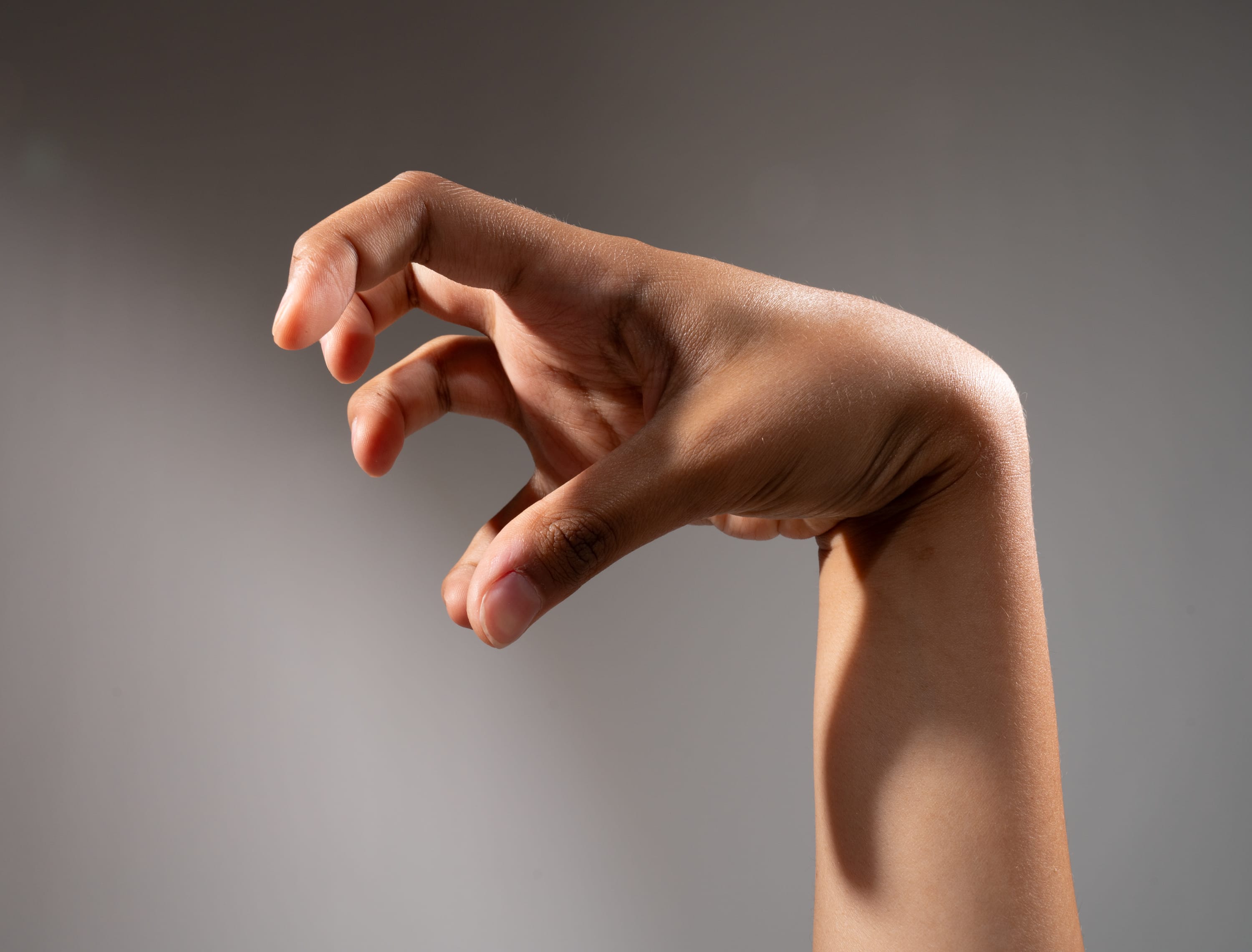 a hand posed as if it were a claw against a grey background.