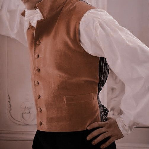 a man is wearing a brown waistcoat over a white shirt with a striped lining. the waistcoat has buttons down the front and a pocket on the right side. he is posing with his hand on his hip. the image is a closeup of the man's torso and the waistcoat. the image is taken indoors and the lighting is soft. the overall tone of the image is elegant and formal.