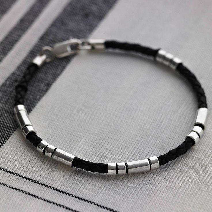 a black leather bracelet with silver beads on a white and black striped background. the bracelet is a minimalist design with a simple clasp. the bracelet would be a great accessory for men.
