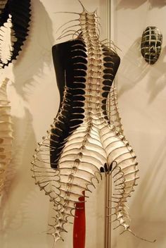 a closeup shot of a white and gold skeletal dress, featuring intricate details and a design that resembles a ribcage or spine. the dress is displayed on a mannequin against a light background, highlighting its intricate details and unique design.