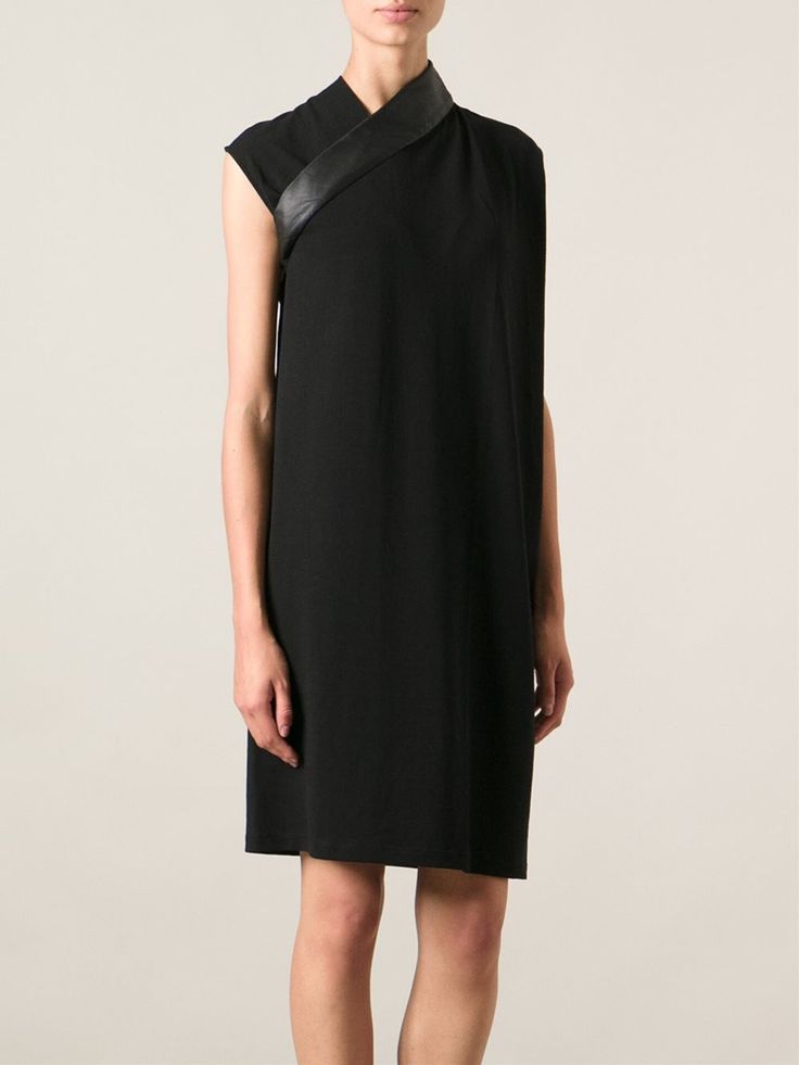 a woman is shown wearing a short, black, sleeveless dress with an asymmetrical, tunicstyle design, highlighted by a wide leather strap around the neck and over the shoulder.