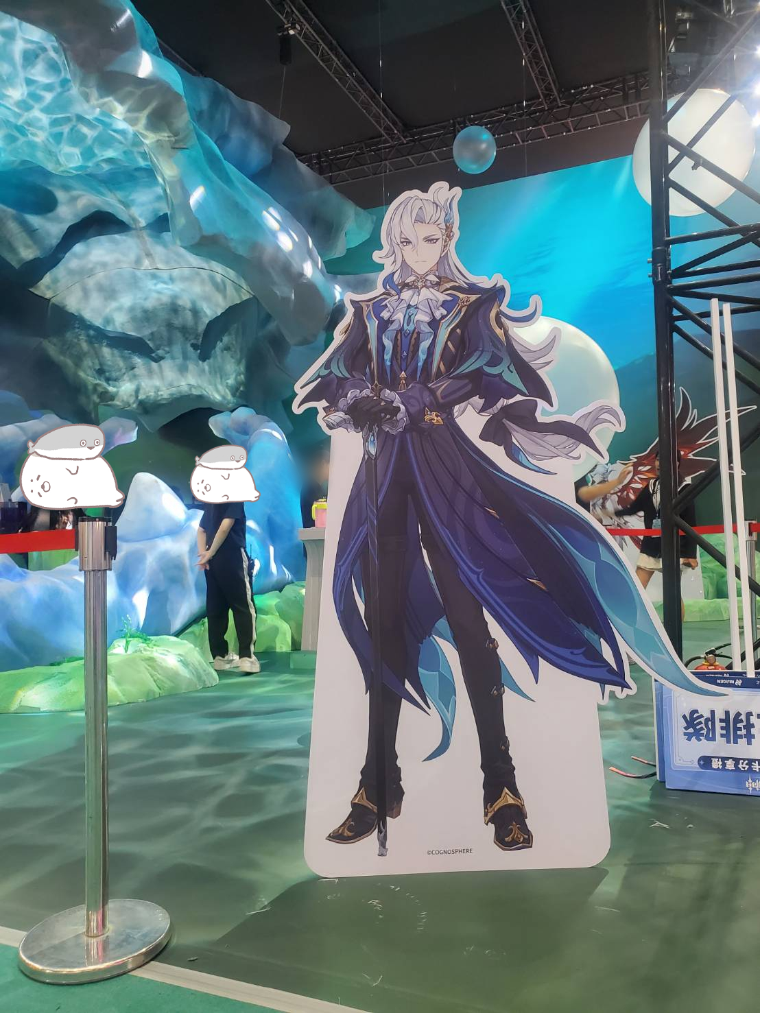 an image of a cardboard cutout of albedo from genshin impact. the cutout is at a genshin impact event with a blue background and the cutout is surrounded by a blue and white backdrop with a green grassy floor in front.