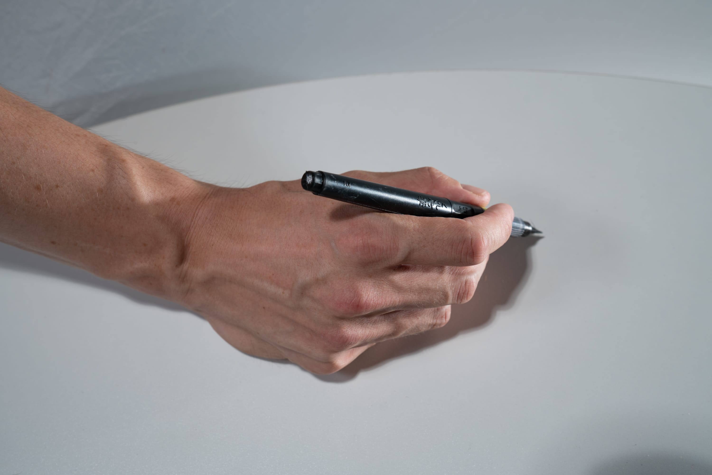 a man's hand holding a pen over a white table.