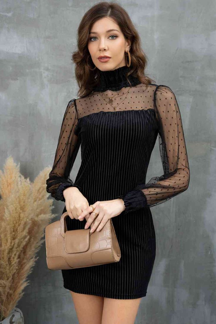 a brunette woman is posing in a black velvet dress with a mesh polka dot overlay. she's holding a brown clutch bag.
