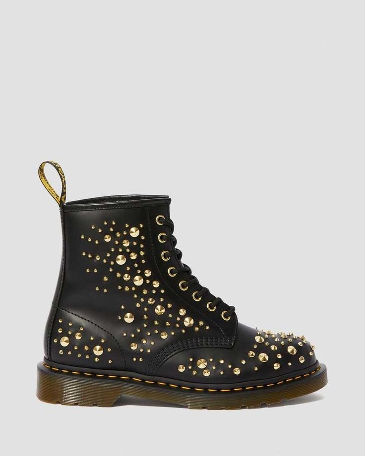 a pair of black leather combat boots with gold studs on the upper and laces. the boots are laceup and have a thick, black rubber sole. they are a classic doc martens style, but with a punk rock twist. the boots are very eyecatching and would be a great addition to any edgy outfit.
