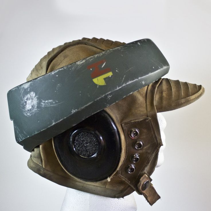 a closeup side view of a worn rebel pilot helmet. the helmet is made of brown leather and has a green visor that can be flipped up. the helmet also has a small emblem on the top. the helmet appears to be from the star wars universe.
