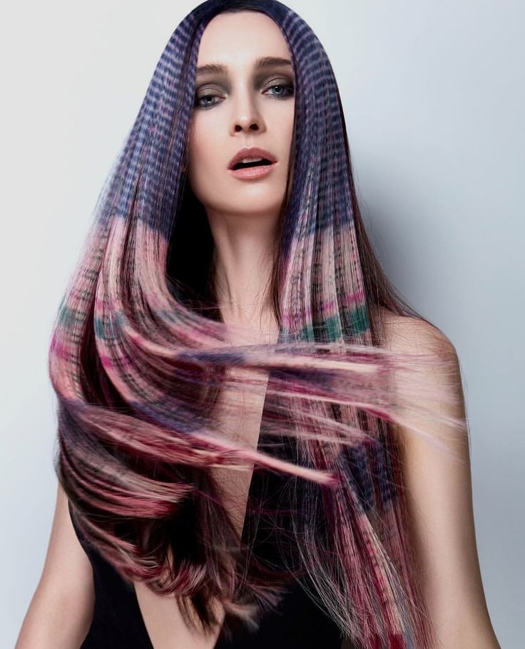 a woman with long dark hair with streaks of pink, blue, purple and green running through it. her hair is styled so that it flows out from her face and down her back. she is wearing minimal makeup and has a serious expression.