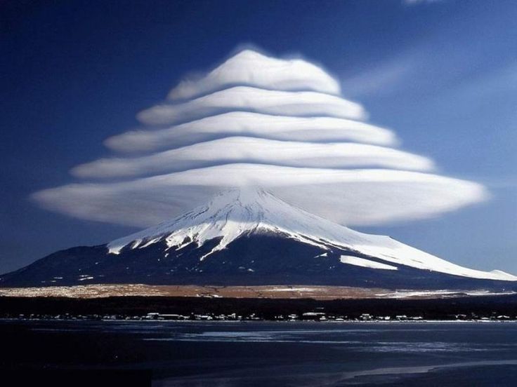 a stunning image of mt. fuji, japan, with a lenticular cloud formation hovering above. the cloud formation is perfectly symmetrical, creating a striking visual effect. the mountain is covered in snow, and the sky is a deep blue. this photo is a beautiful example of the power and beauty of nature.