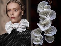 a woman wearing a black dress with white polka dots and a large white collar. she has a elegant style. on the right side of the image, a delicate, white, lacelike flower arrangement is shown. the image is taken in a studio setting. the woman is looking at the camera.