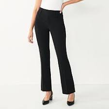 a woman is wearing black pants and a white shirt, she is standing and looking down. she is wearing black shoes. the picture shows a woman in formal clothing ready for work or a business meeting.