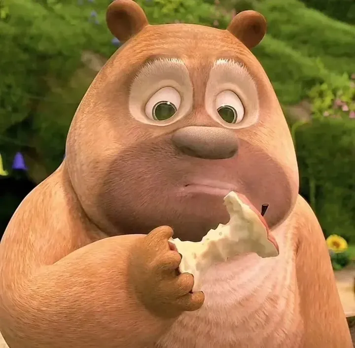 a closeup shot of an animated bear with brown fur eating an apple. the bear's expression is slightly melancholic. the background is blurred and suggests a lush outdoor environment.