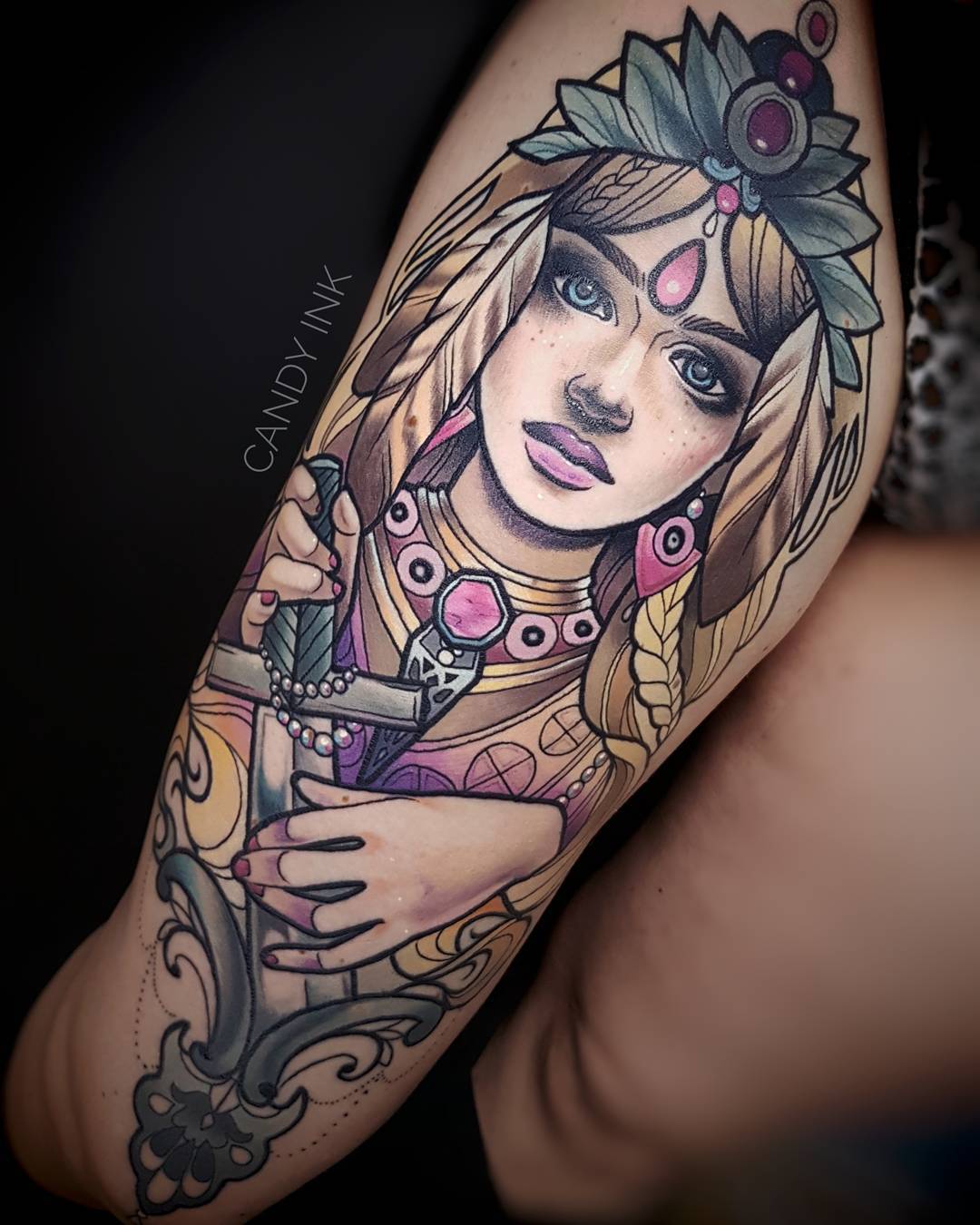 a neo traditional style tattoo of a woman holding a sword. she has blonde hair, fair skin and is wearing a crown and jewelry. the tattoo is on someone's upper arm.