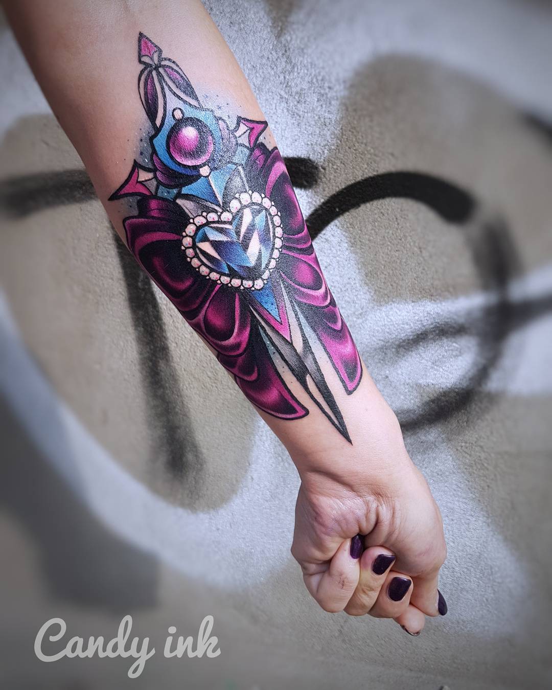 a person's lower arm with a colorful tattoo of a jeweled dagger piercing a heart and bow. the tattoo is in the style of candy ink. the photo is taken indoors under artificial lighting. the perspective is from the side.