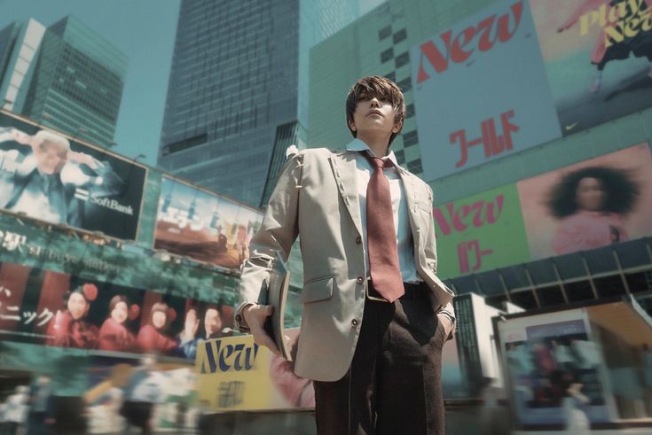 a lowangle, medium shot of a person cosplaying as light yagami from the anime death note. they are dressed in a beige suit and red tie, standing in a bustling urban environment filled with tall buildings and large billboards. the background is blurry, creating a shallow depth of field that emphasizes the cosplayer.  the overall style suggests a blend of japanese and western urban aesthetics.