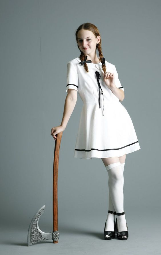 a young woman in a white dress and white thighhigh socks stands with her right hand resting on a large axe. she's also wearing black heels and has her hair styled in pigtails.  the background is solid gray.