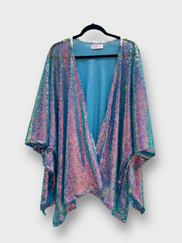 a blue iridescent sequined kimono with an open front. the kimono is draped over a hanger, and the sequins are catching the light and reflecting in a variety of colors.  the garment is a halter style top, the neckline is low cut.  it appears to be a glamorous, partyready piece of clothing.