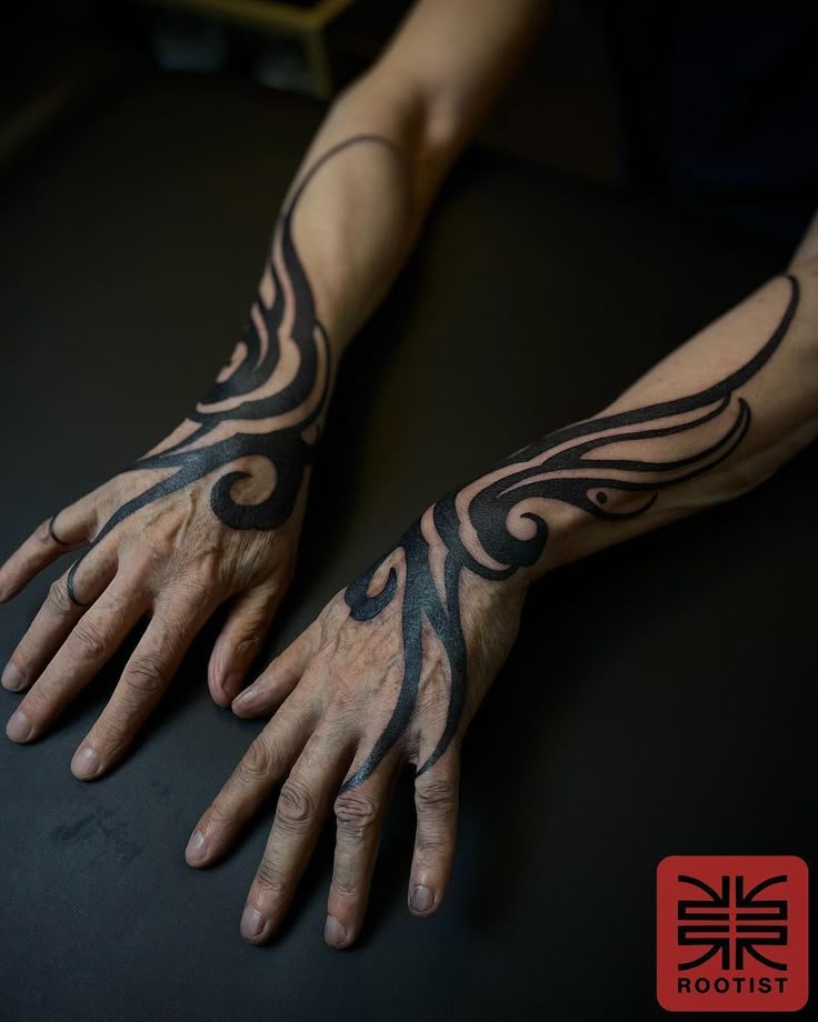 the image shows two hands with tribal tattoos that extend onto the forearms. the tattoos are in black ink and have a swirling, fluid design. the hands appear to belong to an older person due to the visible wrinkles and skin texture. in the bottom right corner, there is a logo that says "rootist". the background is a dark surface.