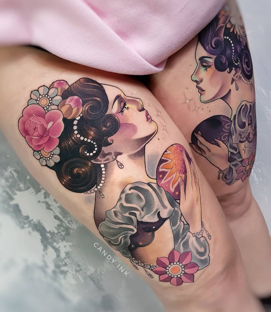 a person's thighs with neo traditional style tattoos of the side profiles of two women with flowers in their hair holding a planet and a crystal ball. the tattoo is by the artist candy ink.
