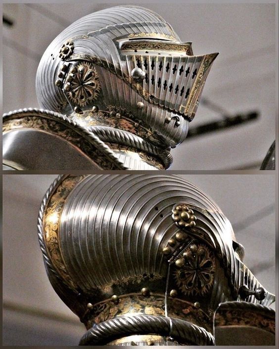 the image is a closeup view of a highly ornate medieval helmet and the upper portion of its accompanying suit of armor. the helmet is made of polished steel with gold accents and detailing.  the top of the helmet features fluted metalwork that transitions into a more elaborate design around the visor and neck guard. the visor has small, evenly spaced cutouts, and there are decorative floral motifs and patterns engraved into the metal. the armor in the lower portion of the image continues the intricate craftsmanship with similar detailing. the lighting highlights the polished surfaces of the metal and emphasizes the intricate designs. the background is blurred, indicating the helmet is likely on display in a museum.