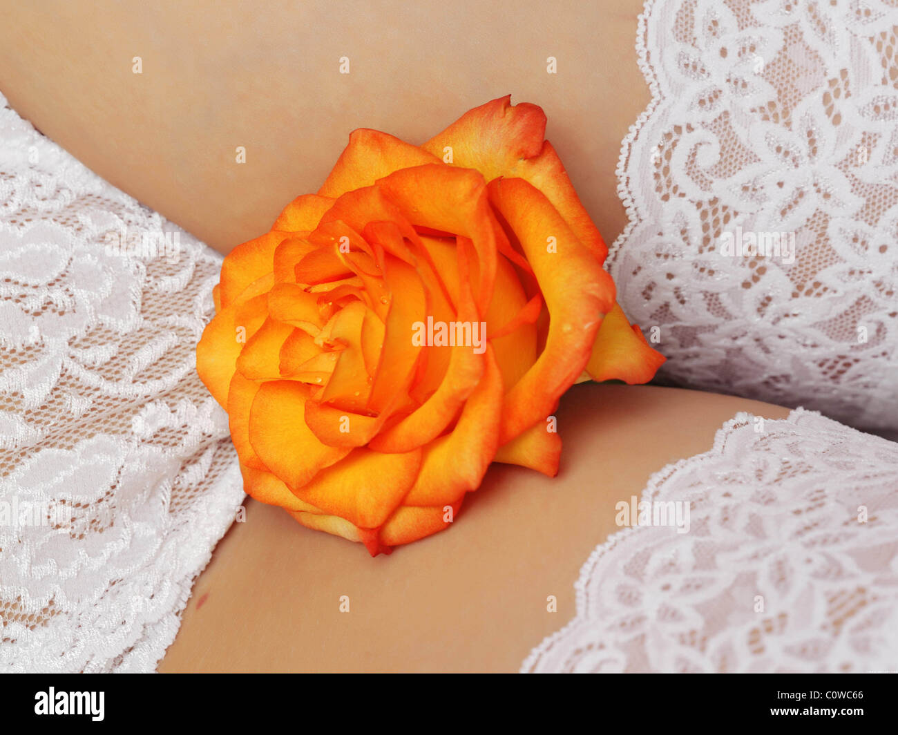 loseup view of a vibrant orange rose resting on the abdomen of a woman wearing white lace lingerie. the focus is sharp on the rose and the lace, showcasing the textures and colors. the overall mood is sensual and romantic.