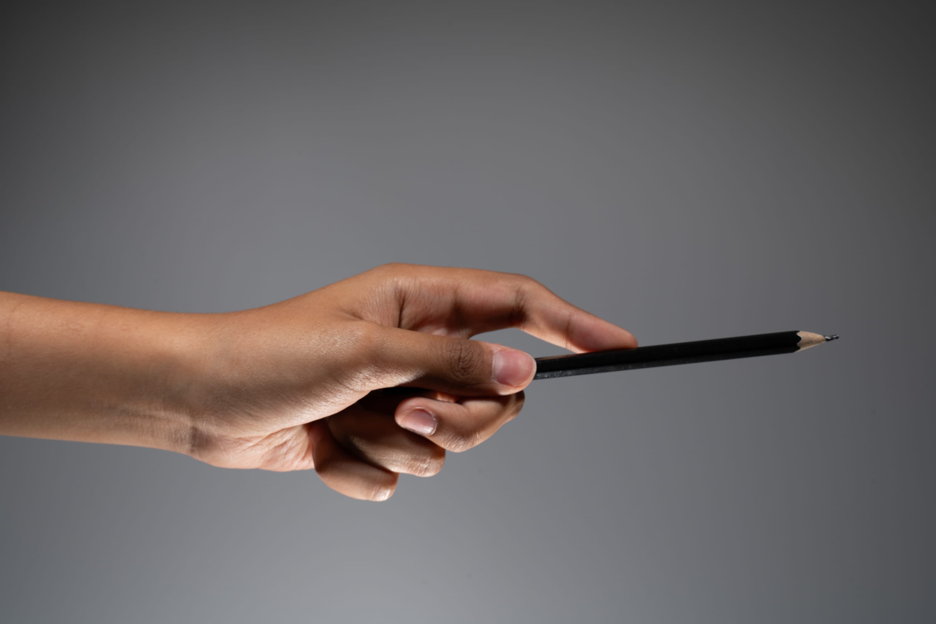 a hand holding a black pencil against a gray background.