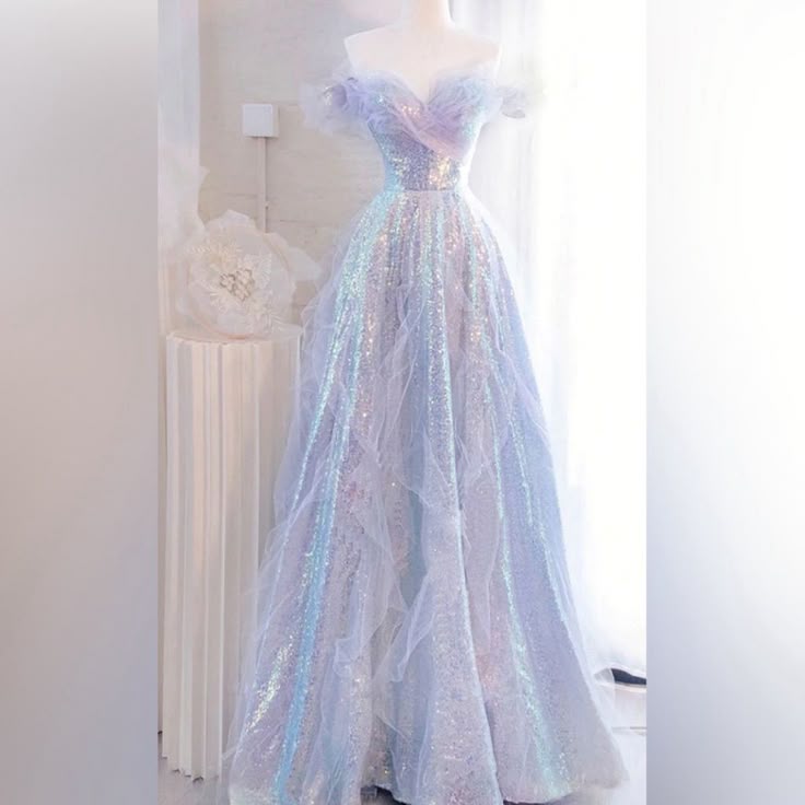 a mannequin displays a long, iridescent gown with an offtheshoulder design. the dress is adorned with sequins and layers of tulle, creating a dreamy and ethereal effect. the pastel color palette and flowing silhouette suggest it could be a wedding dress or prom dress.