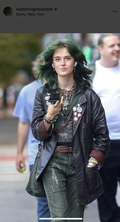 a stylish woman with green hair walks on the streets of soho, new york city. she is wearing a black leather jacket, green jeans, a black bag, and many accessories, creating a trendy look. the image captures a cool and casual street style.