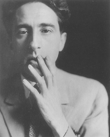 the image is a closeup, black and white portrait of a young man. he appears to be from the 1920s or 1930s, judging by his clothing and hairstyle. he is wearing a lightcolored suit with a subtle texture.  his expression is serious and thoughtful, almost pensive. his hand is raised to his mouth, partially covering his lips. the lighting is dramatic, creating a strong contrast between light and shadow, typical of studio portraits from this era. the background is dark and indistinct, drawing all attention to the subject. the overall mood is one of quiet intensity and contemplation.