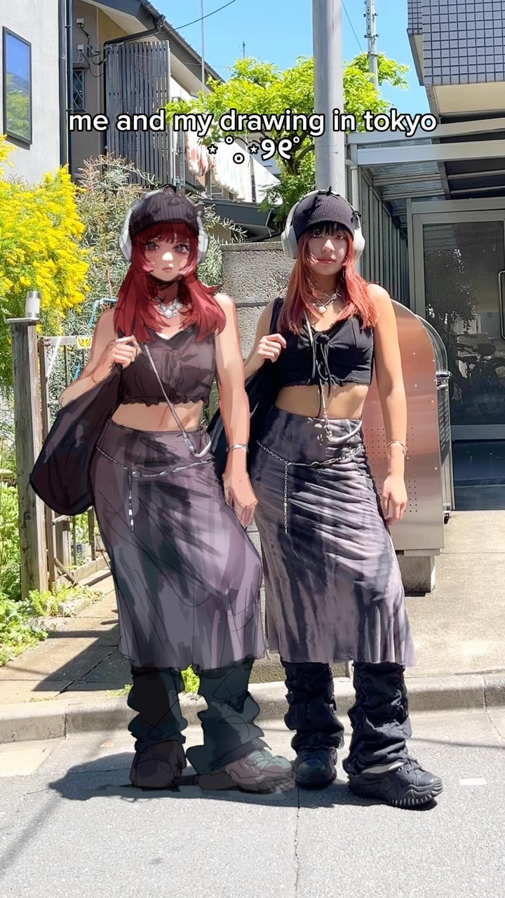 the image shows two girls in tokyo, japan. one is a real person, and the other is a drawing of an anime character. they are dressed in similar outfits, with long skirts and dark boots, and are posing together on a city street. the image is bright and cheerful, and captures the fun energy of the moment. the text overlay says "me and my drawing in tokyo".