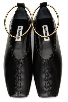 a pair of black leather jil sander ballerina flats with gold rings on the ankles.